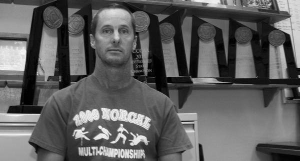 Coach Rick Anderson stands in front of the many trophies won over the years. (Photo by Bryce Fraser)