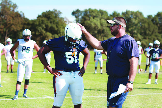 New Head coach Jon Osterhout explains the details of a play to the football team during the first practice of the season. (Photo by Emily K. Rabasto)