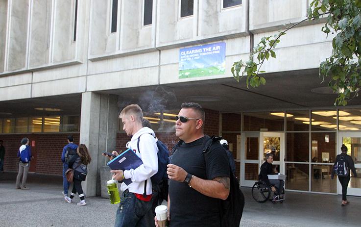 Matt Paiva smokes a cigarette in front of Davies Hall beneath a sign alerting students to the change in American River College policy that will ban tobacco use effective Jan. 1. (Photo by John Ferrannini)