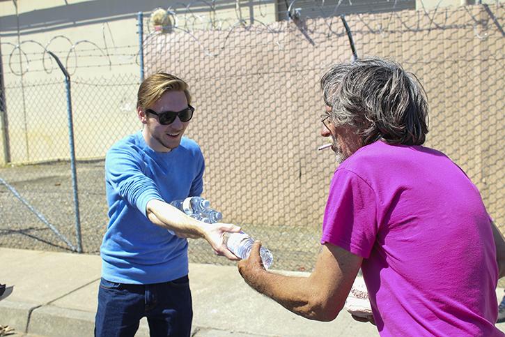 American River College Film Club president Vince Blake (left) hands a water bottle to a homeless man near Loaves and Fishes in Sacramento. Blake, 19, said he hopes to get more ARC students involved with helping out over time. (Photo by Timon Barkley)