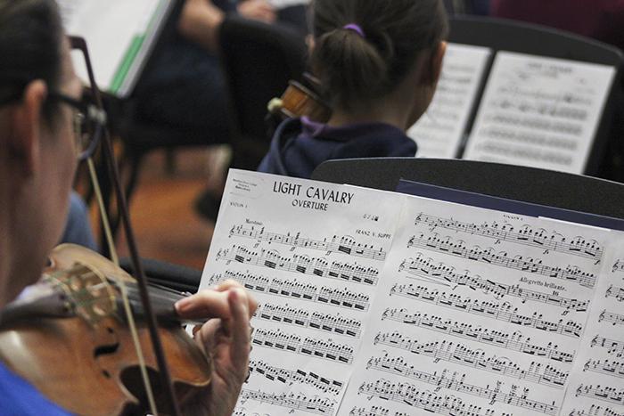 The sheet music for Light Cavalry Overture by Franz von Suppe is seen over the shoulder of a violin player from the American River College Orchestra at their March 30 practice. The orchestra recently welcomed four primary school musicians to their practice. (Photo by Hannah Darden)