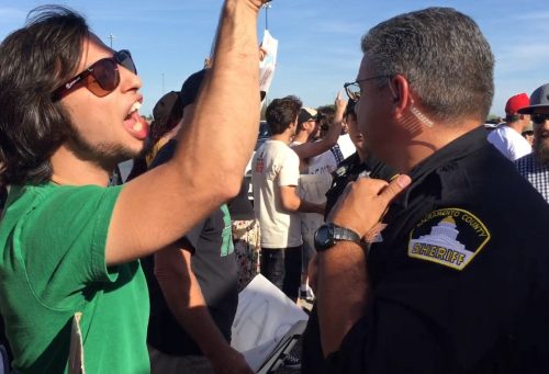A protester shouts over a police officer at Trump supporters as the file into Trump's rally in Sacramento. (Photo by Jordan Schauberger)