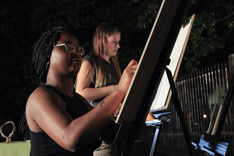 American River College Art Club members Aerial Sudds (left) and Brianna Hulce (right) work on paintings at the live art show and open mic night at Oak Park Brewing Company in Sacramento, California on Sept. 6, 2016. The art club attended the event to make and sell art in the community. (Photo by Hannah Darden)