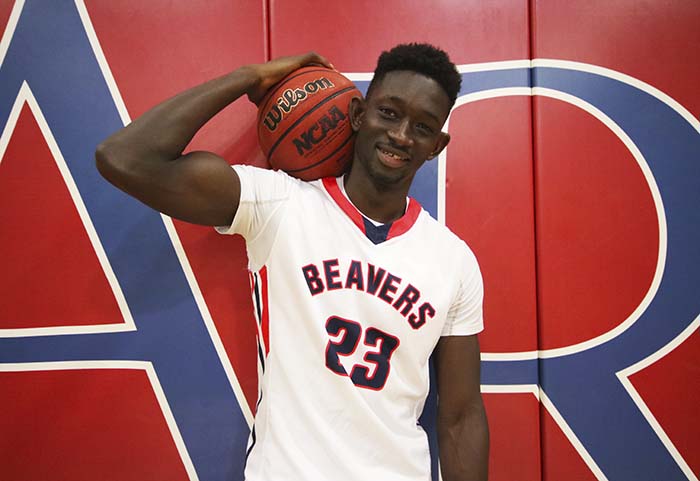 Freshman Wing Baidi Kamagate holds a basketball in front of an ARC sign in the small gym. Kamagate said that his mother and father have been a huge influence on his life and supported him in his decision to move from Africa to America on his own. (Photo by Cheyenne Drury)