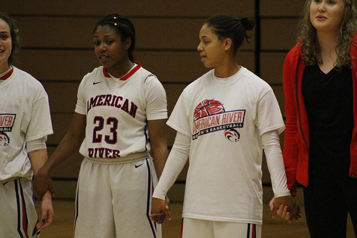 Alana Myers (left) and Deja Samuels (right) join hands during the national anthem before the game starts. (Photo by T.J. Martinez)
