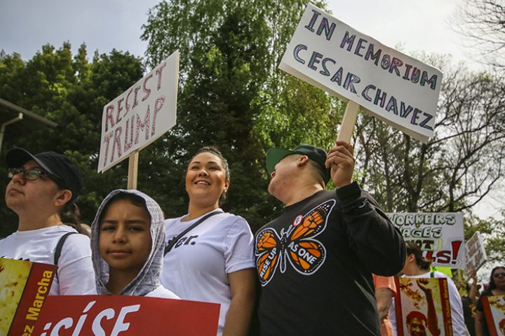 A family walks together during the Cesar Chavez march, holding signs that said, “Si Se Puede’, ‘Resist Trump’ and ‘In Memory of Cesar Chavez’. March 31, 2018 (photo by Brienna Edwards)