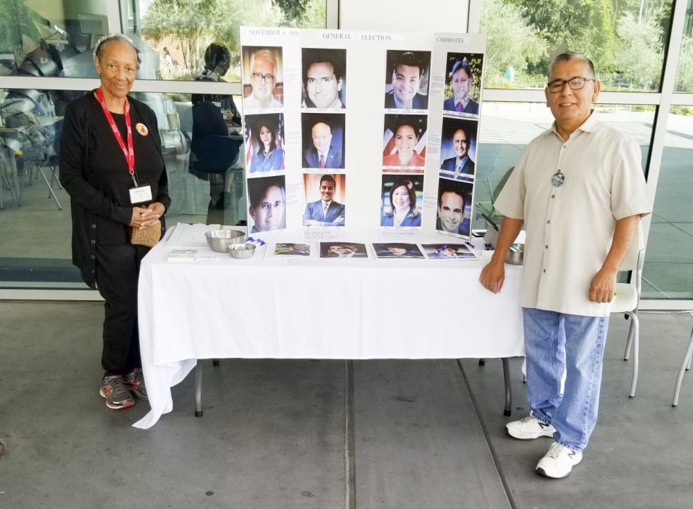 Volunteers Gloria Powell (left) and Issac Rodriguez, from the League of Women Voters, stand next to their display that encourages college students to register to vote at American River College on Sept. 4, 2018. (Photo by Christian Sutton)