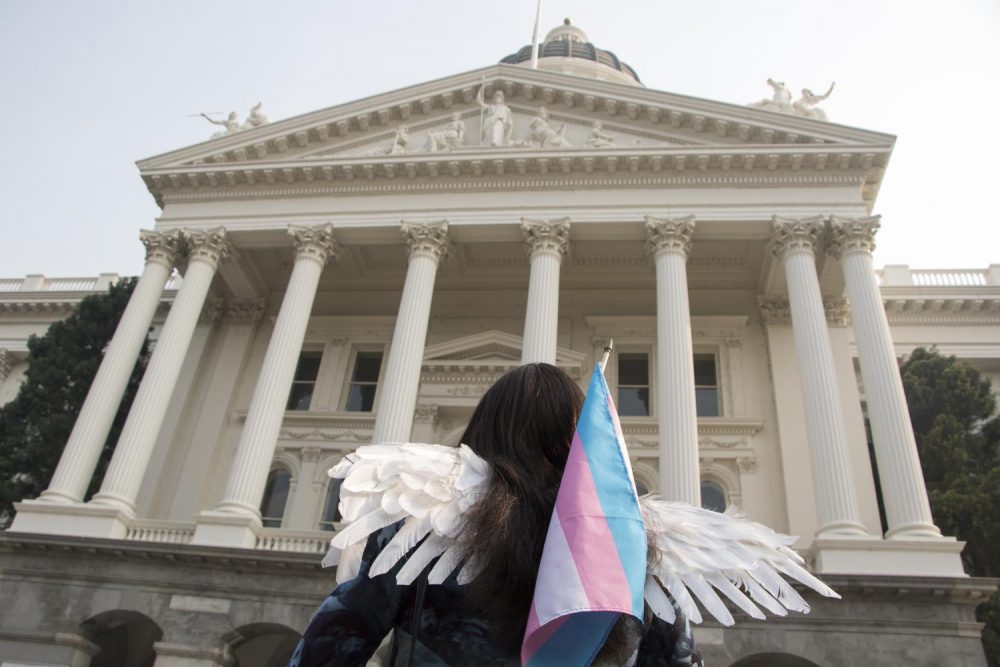 A protester carries a transgender pride flag and wears angel wings during the #StillHere Capitol March & Rally for Trans Justice at the California State Capitol in Sacramento, Calif. on Nov. 10, 2018. The wings symbolize the many transgender women who have been murdered. (Photo by Ashley Hayes-Stone) 