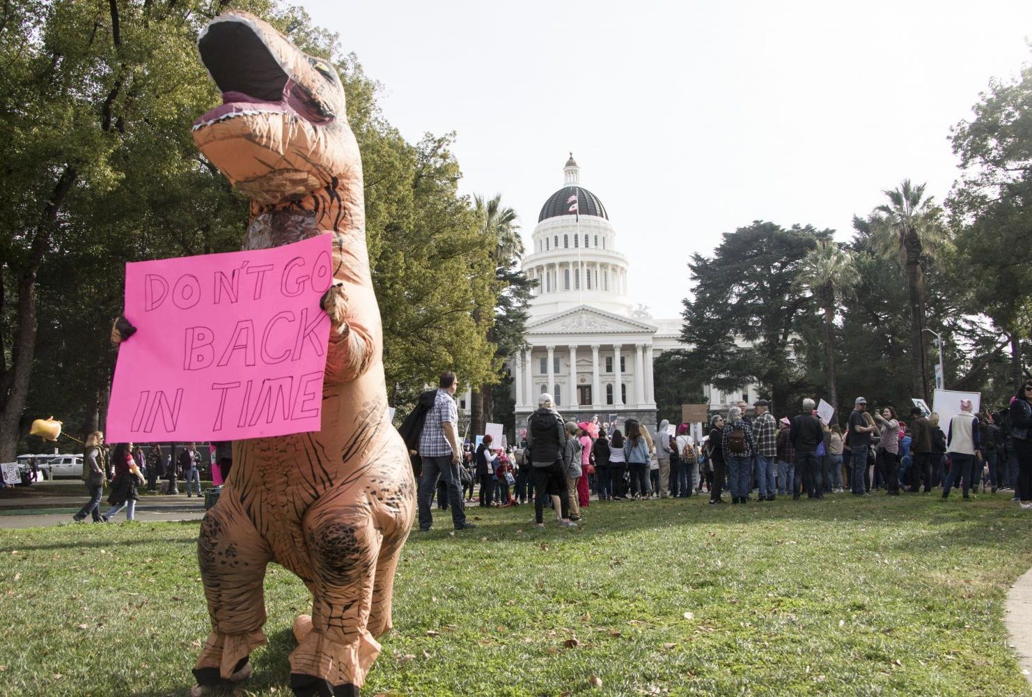 A demonstrator dressed in a dinosaur costume holds up a sign that reads “Don’t Go Back In Time” in front of the California State Capitol during third annual Women’s March in Sacramento, Calif. on Jan. 19, 2019.