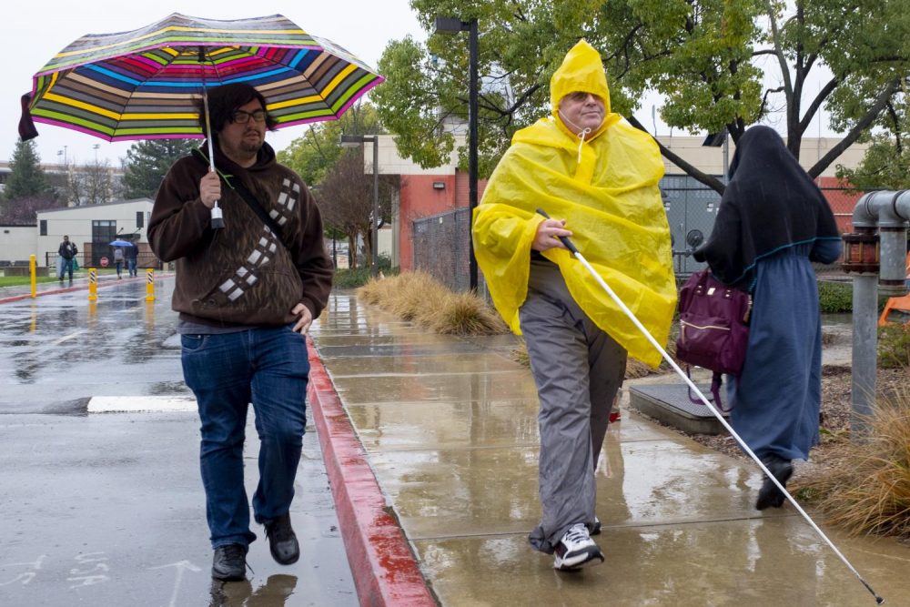 History major Jordan Alberti and human services major Paul McIntyre make their way across campus in the rain underneath an umbrella and inside a poncho on Feb. 26, 2019. (Photo by Patrick Hyun Wilson)