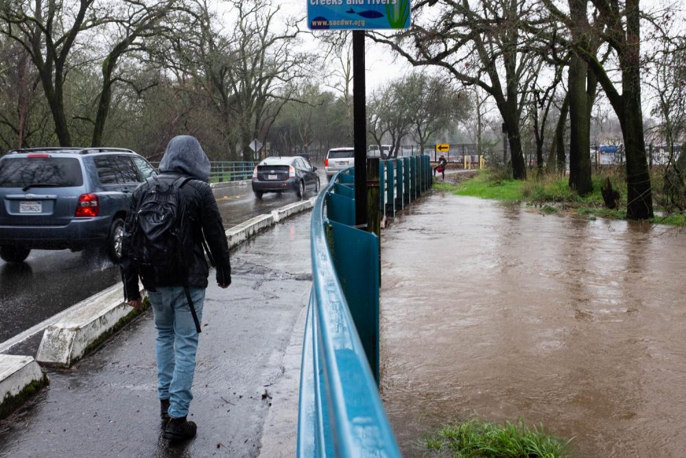 A student walks across the bridge over Arcade Creek as rain causes the creek to flood nearly over the ridge at American River College on Feb. 26, 2019. (Photo by Patrick Hyun Wilson)