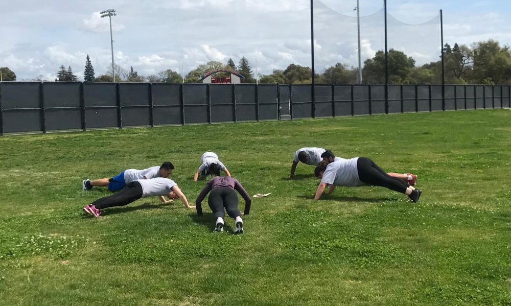 Students in the Boot Camp Fitness class, a class dedicated to putting students through various forms of exercise including strength and endurance training, do pushups as part of their workout near the tennis courts at American River College on March 28, 2019. (Photo by Alexis Warren)