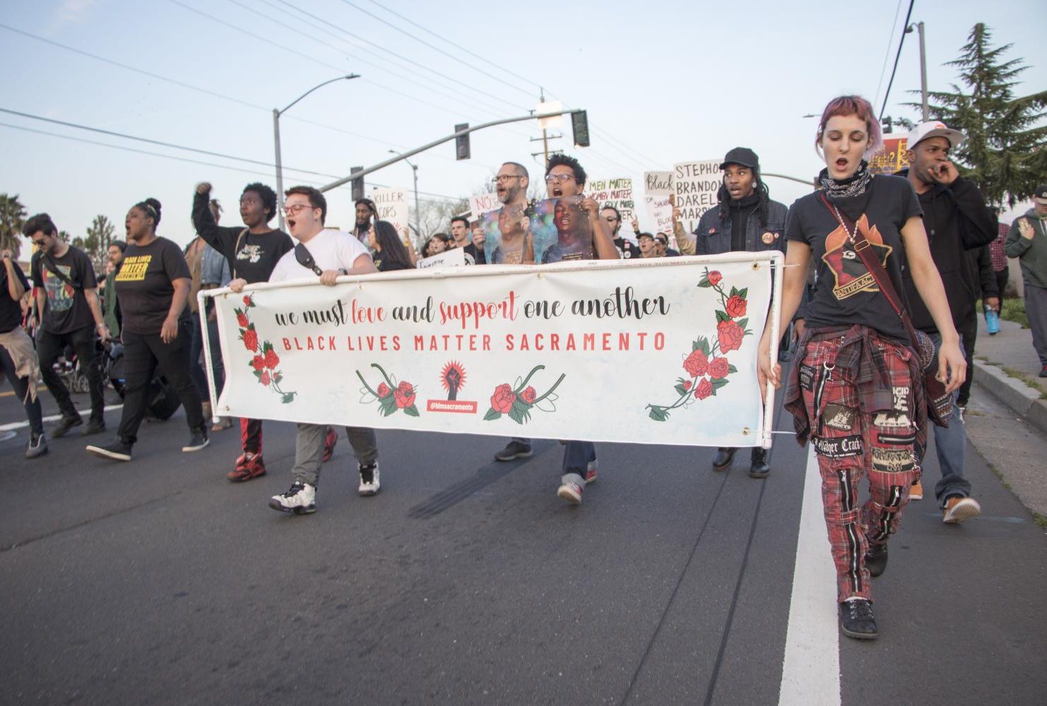 Demonstrators hold up a sign that reads “We must love and support one another / Black Lives Matter Sacramento” banner during the one year anniversary of Stephon Clark’s death in South Sacramento, Calif. on March 18, 2019. (Photo by Ashley Hayes-Stone)
