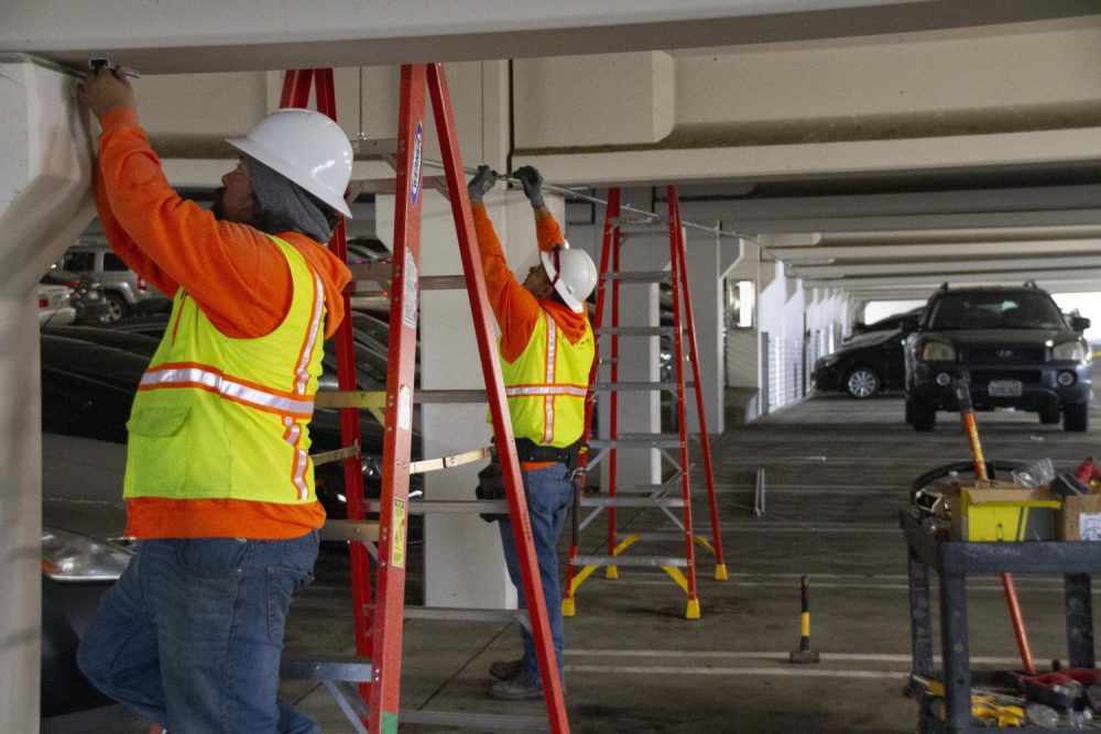 Derrick Camero and Billy Johnson, construction workers from Sebastian Corp, install security cameras in the parking structure as a part of a district wide update at American River College on April 2, 2019. (Photo by Jennah Booth)