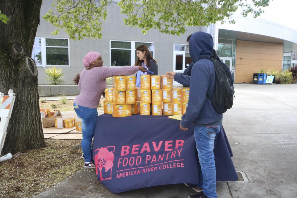 Mariama Bah and Ana Radu, student support specialists for the American River College Beaver Food Pantry, distribute cheddar flavored Blue Diamond Nut-Thins to students on March, 17 2020. This will be the last day that the food pantry will operate before the campus closes indefinitely due to the COVID-19 pandemic.  (Photo by Oden Taylor)