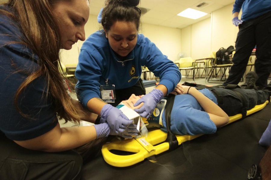Anysia Hernandez, an EMT program major, simulates a cervical immobilization on a stretcher that is made for trauma patients. This photo was taken before the campus shut down on March 18, 2020. (Photo by Emily Mello) 